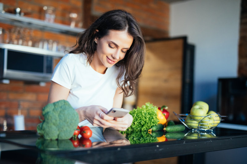 Portrait of her she nice-looking attractive lovely girl reading recipe online on the phone fresh lunch dinner farm organic vegs in light white interior room.