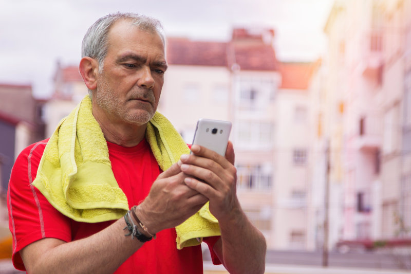 lifestyle portrait of adult man with towel after sport training in gym and using mobile phone